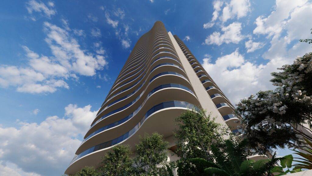 Modern high-rise building against a blue sky with clouds, surrounded by lush greenery.