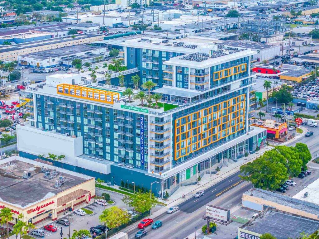 Modern urban landscape with a multi-story building in Allapattah, featuring vibrant geometric designs and a lush rooftop garden.