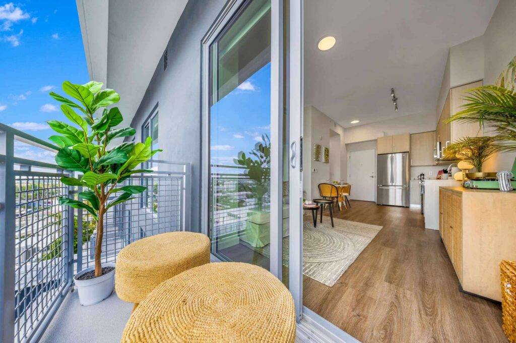 Modern apartment balcony with wicker chairs and a lush potted plant.