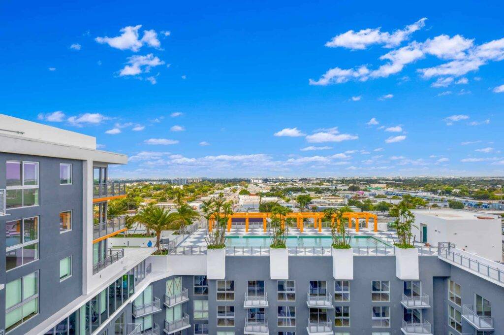 Aerial view of a modern apartment complex with a rooftop pool and city skyline.
