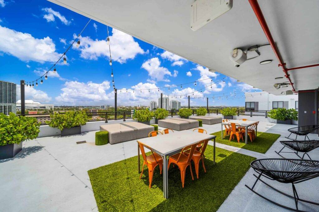 Rooftop patio with orange chairs, tables, and city skyline views under a bright blue sky.