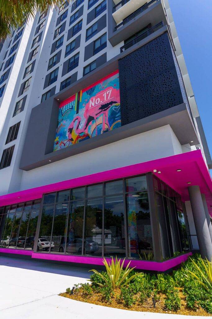 Colorful artwork displayed on a modern high-rise building with large glass windows and vibrant pink accents.