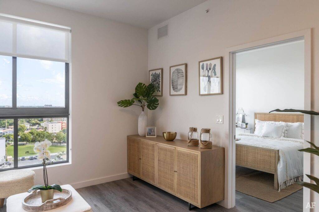 Modern living room with wooden sideboard, indoor plants, and a glimpse into a cozy bedroom.
