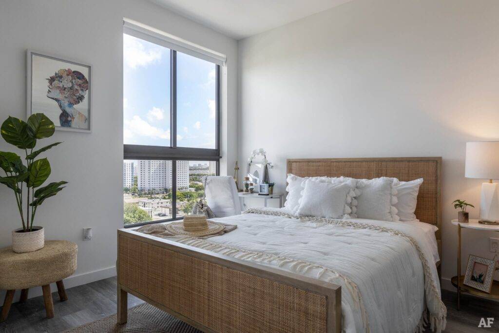 Cozy modern bedroom with a large window, rattan bed, and accent chair in a bright apartment.