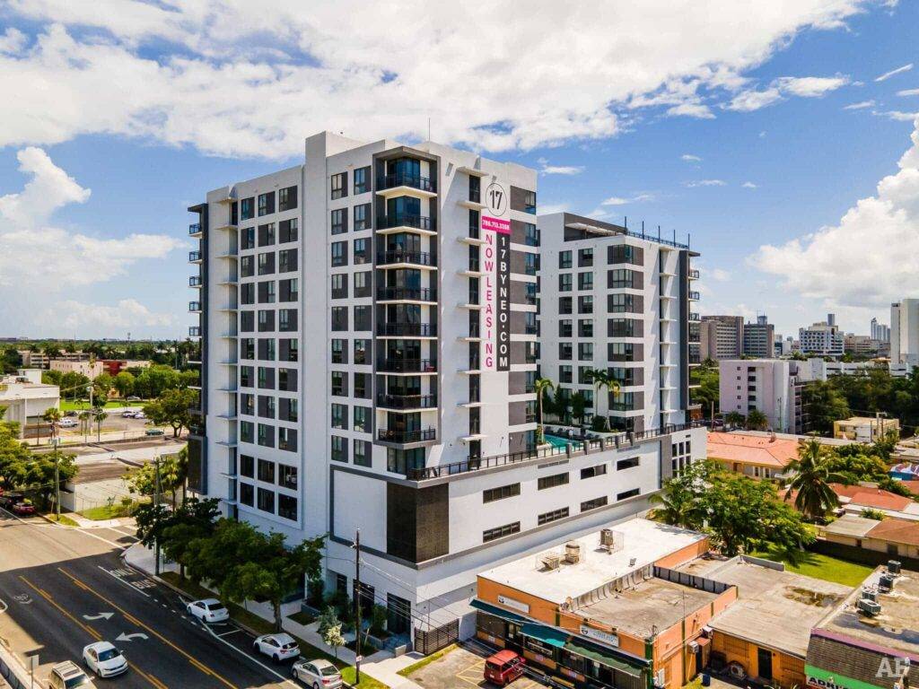 Aerial view of a modern multi-story building in an urban neighborhood with clear skies and surrounding greenery.