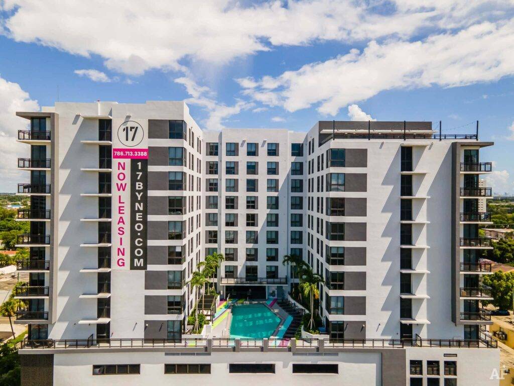 Modern apartment building with rooftop pool and leasing banner.