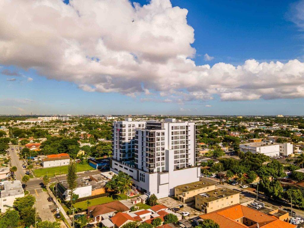 Aerial view of a modern cityscape featuring a tall white building under a partly cloudy sky.