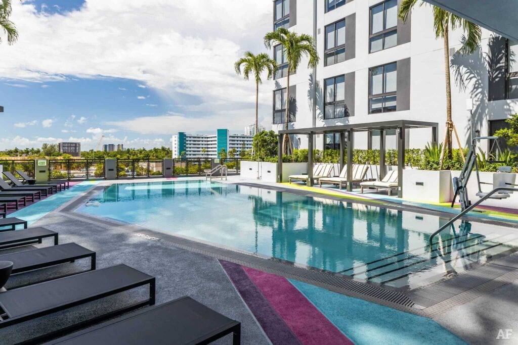Luxurious poolside view with palm trees and modern architecture at an urban apartment complex.