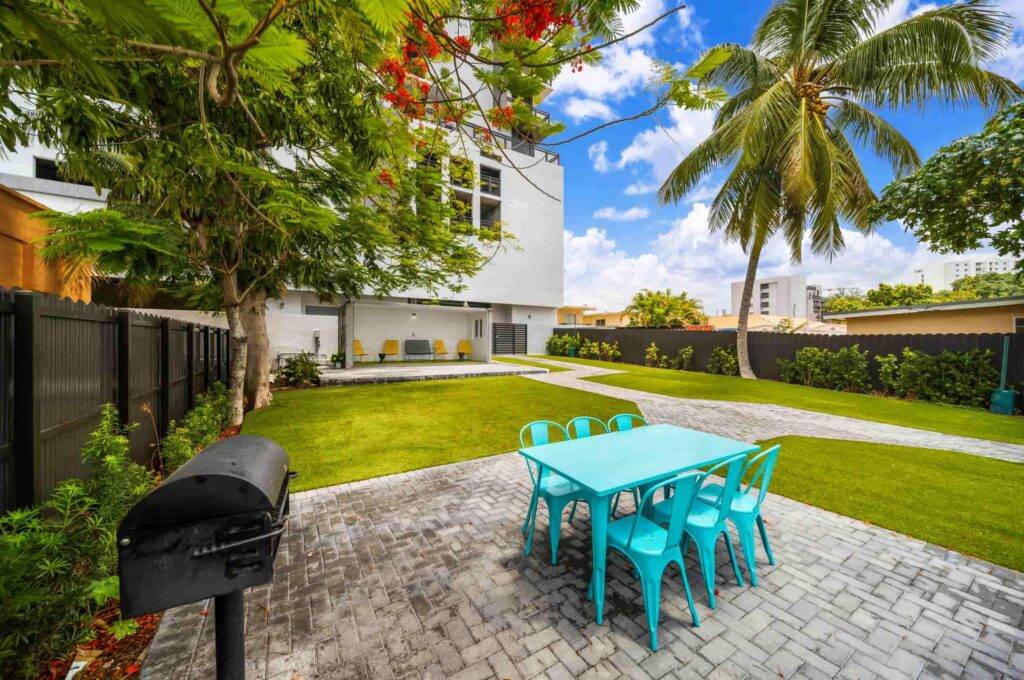 Backyard with turquoise dining set, palm tree, and lush green lawn under a vibrant blue sky.