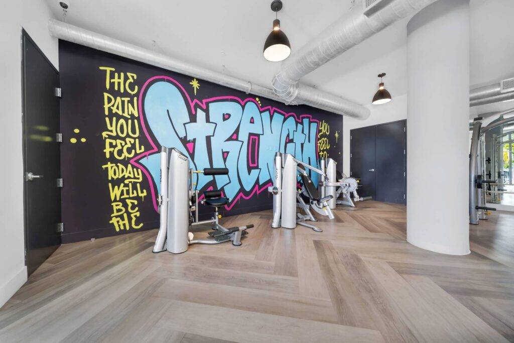 Modern gym interior with vibrant graffiti art on the wall and workout machines.
