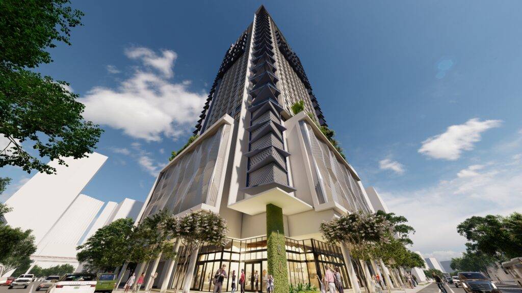 Modern high-rise building with sleek architecture and lush greenery at the base under a clear blue sky.