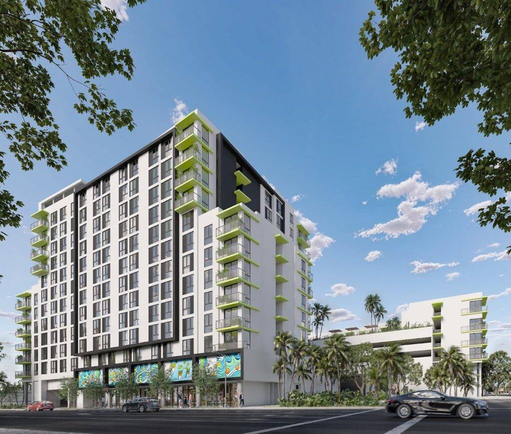 Modern high-rise building with green balconies and surrounding trees under a clear blue sky.