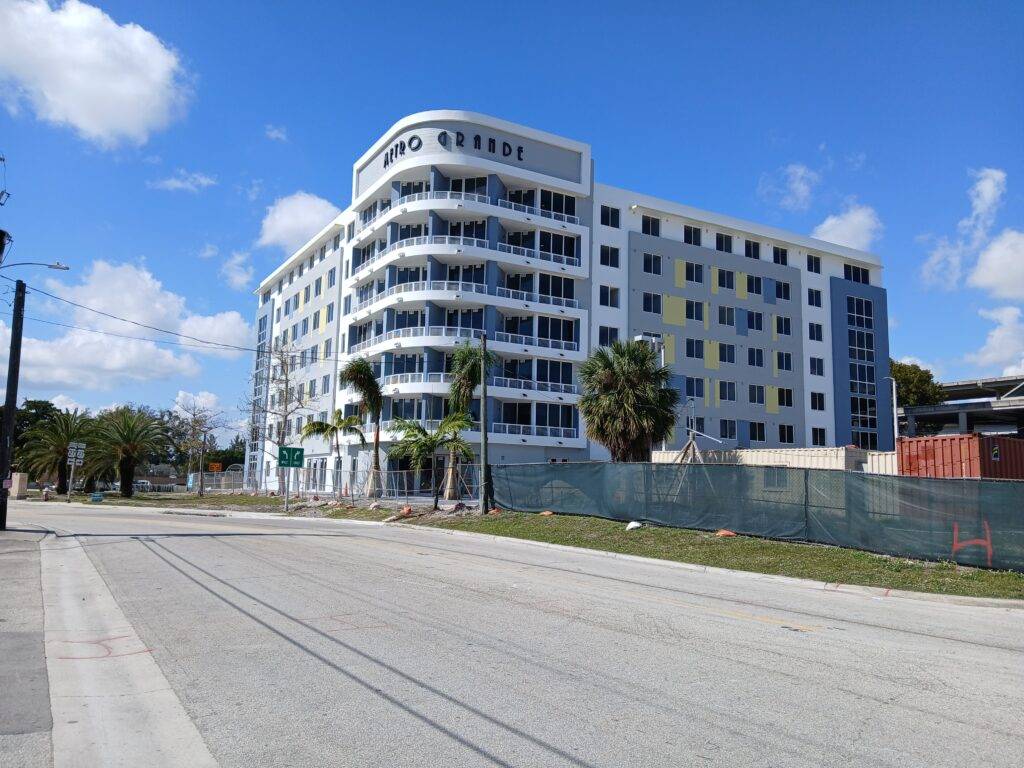 Modern multi-story building with distinctive curved architecture and palm trees, under a bright blue sky.