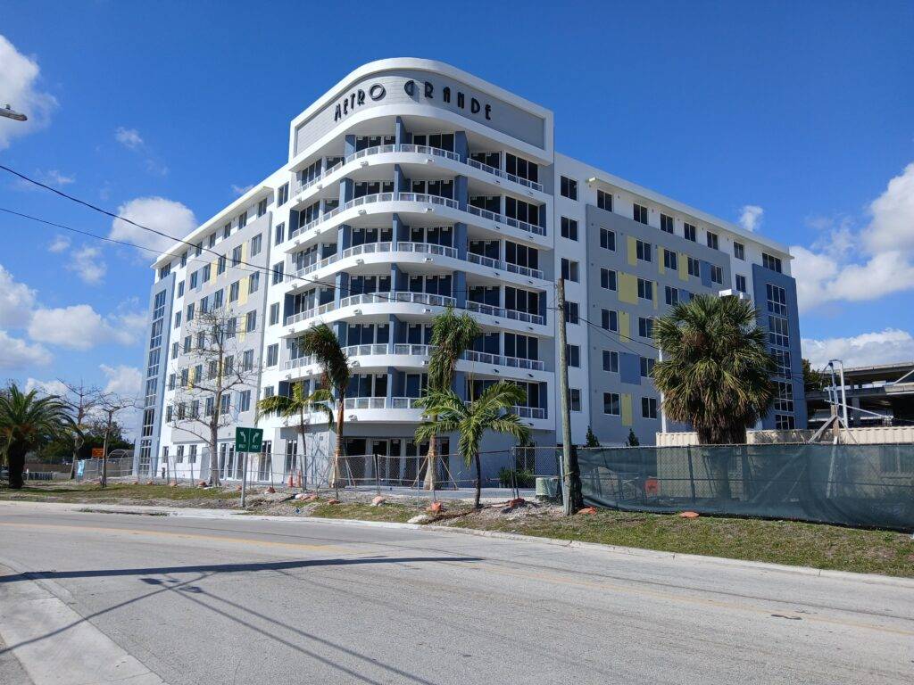 Modern white apartment building with curved balconies and palm trees under a blue sky.