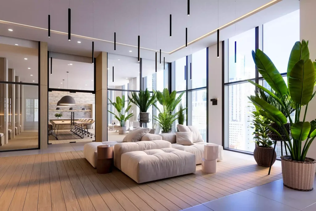 Modern office lounge with white sofas, hanging lights, and lush indoor plants near large windows.
