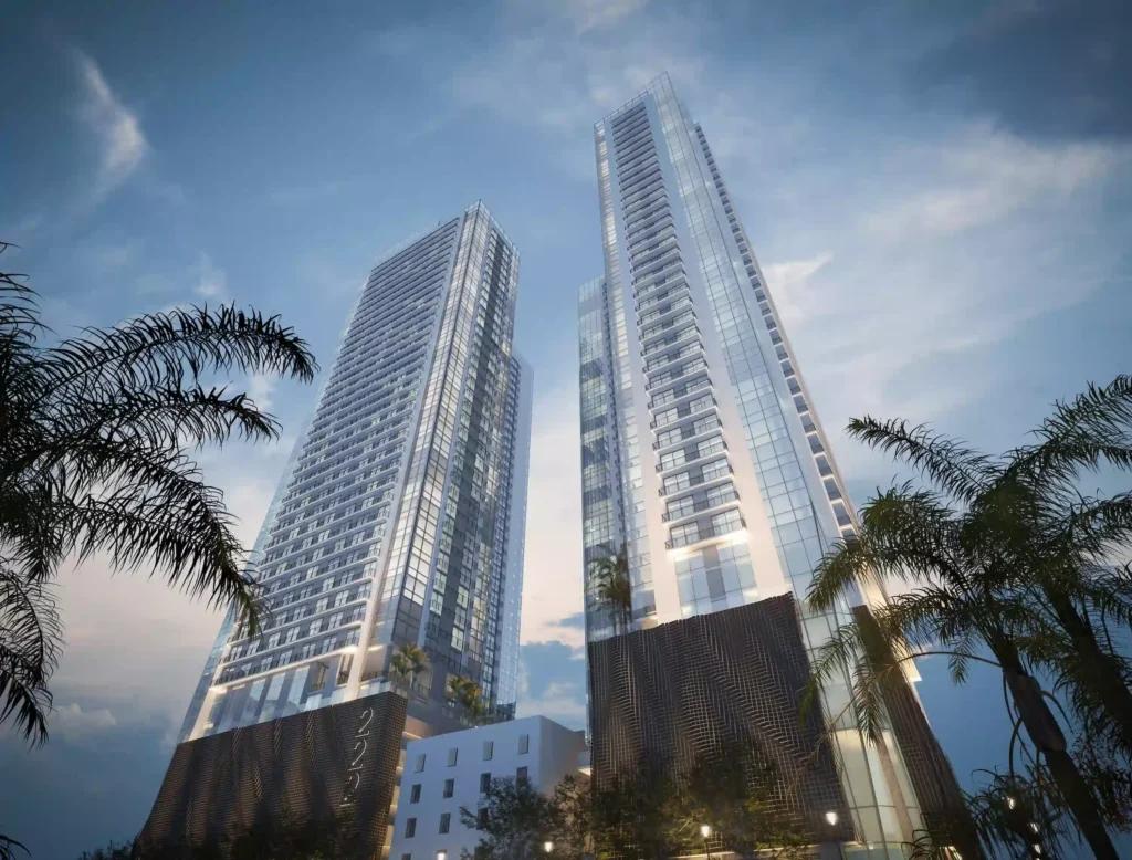 Modern twin skyscrapers surrounded by palm trees under a twilight sky.