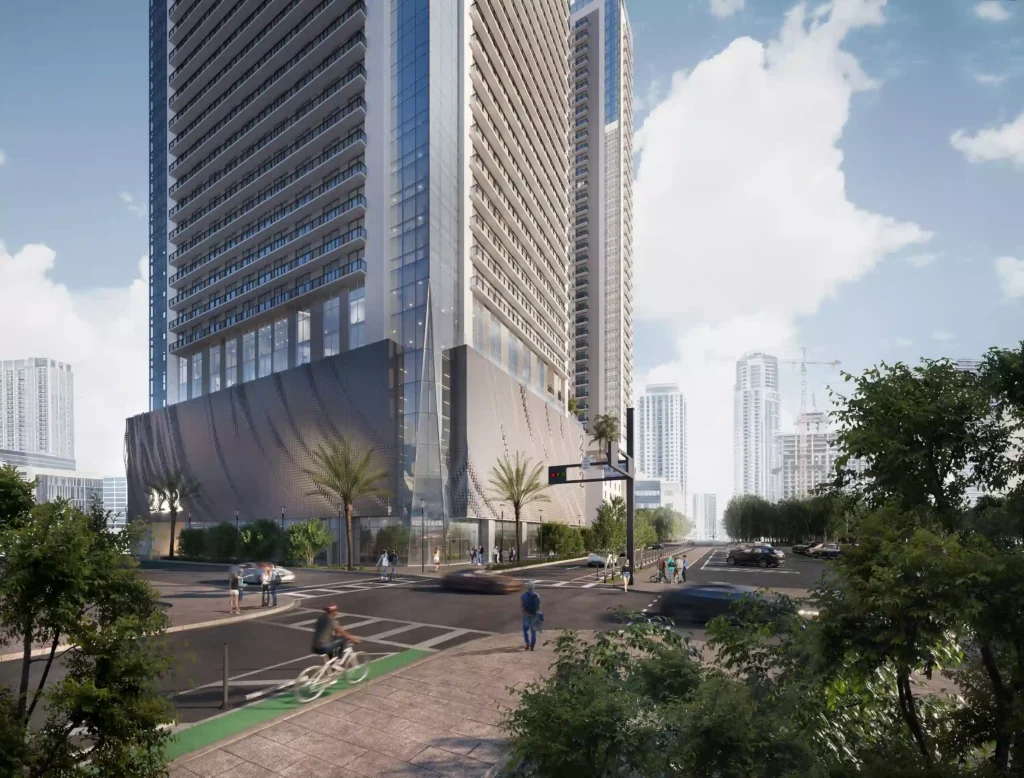 Modern skyscraper against a blue sky with lush greenery and urban street scenery.