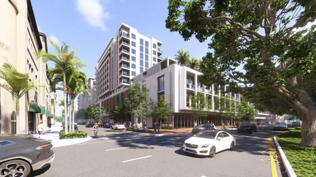 Urban street view with modern buildings, lush greenery, and parked cars under a clear blue sky.