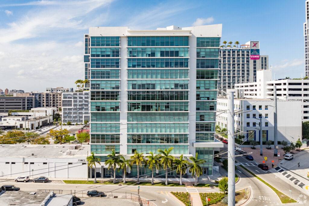Modern glass office building with palm trees in Coral Gables, bright blue sky overhead.