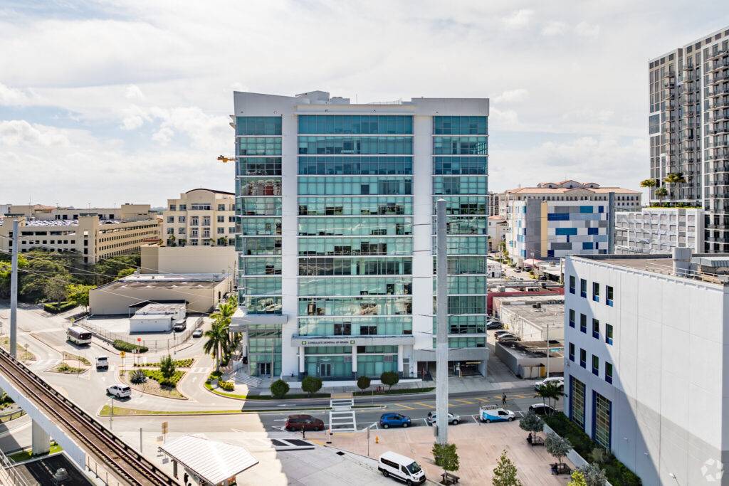 Modern office building with glass facade in Coral Gables, featuring urban surroundings and a clear sky.