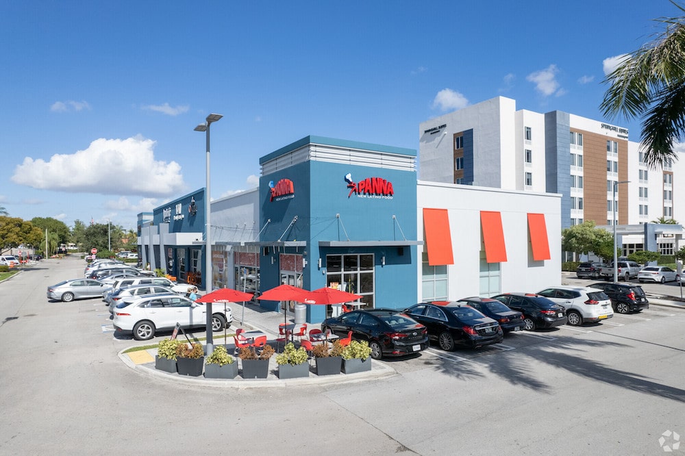 Vibrant shopping center with colorful storefronts and ample parking under a clear blue sky.
