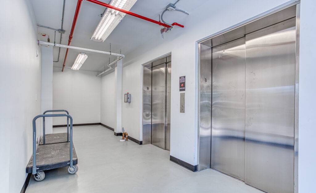 Modern industrial hallway with two stainless steel elevators and a utility cart.