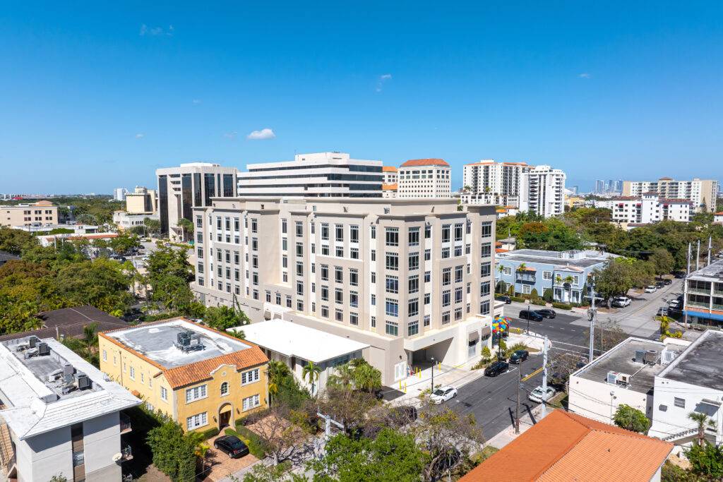 Aerial view of a modern building surrounded by cityscape under a clear blue sky in Coral Gables.