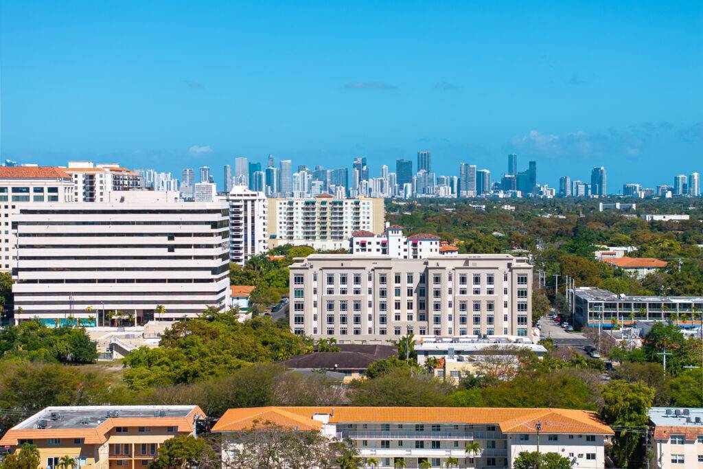 Aerial view of city buildings under a clear blue sky with skyscrapers on the horizon.