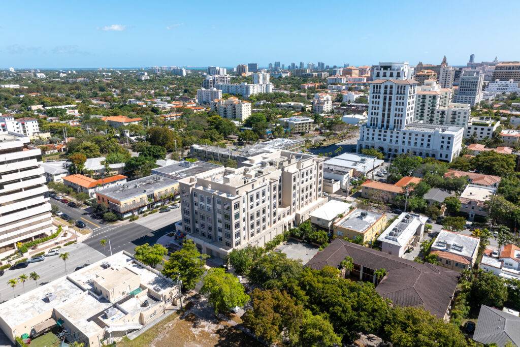 Aerial view of a vibrant cityscape with modern buildings and lush greenery under a clear blue sky.