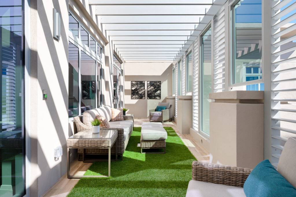 Modern patio with wicker furniture and lush green flooring under a slatted roof.