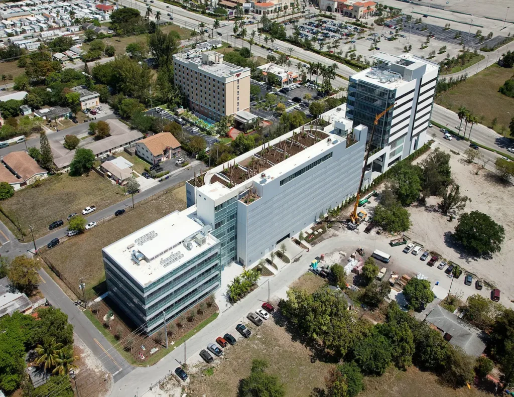 Aerial view of a modern urban building surrounded by trees and parking lots.
