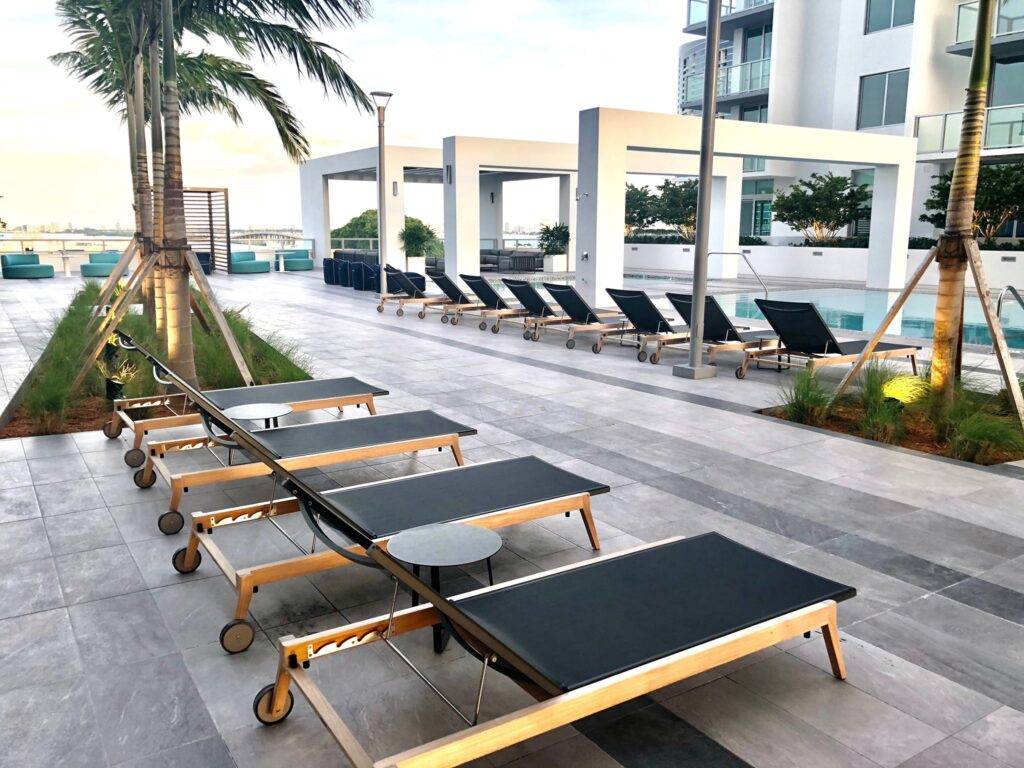 Modern outdoor pool area with sleek lounge chairs and palm trees at a contemporary apartment complex.