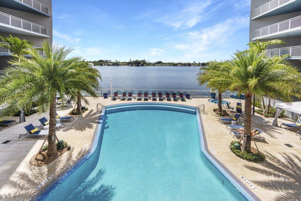 Luxurious tropical swimming pool with palm trees overlooking a serene lake under a clear blue sky
