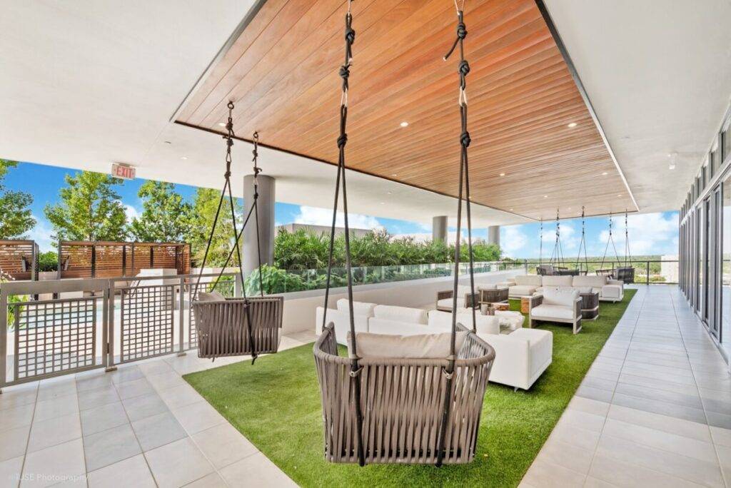 Outdoor lounge with modern furniture and hanging chairs on a terrace with greenery and city views.