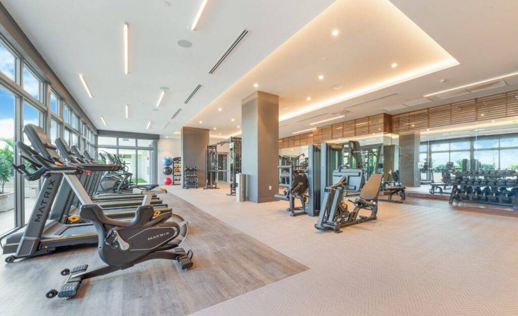 Modern gym with cardio equipment, free weights, and large mirrors in a spacious, well-lit environment.