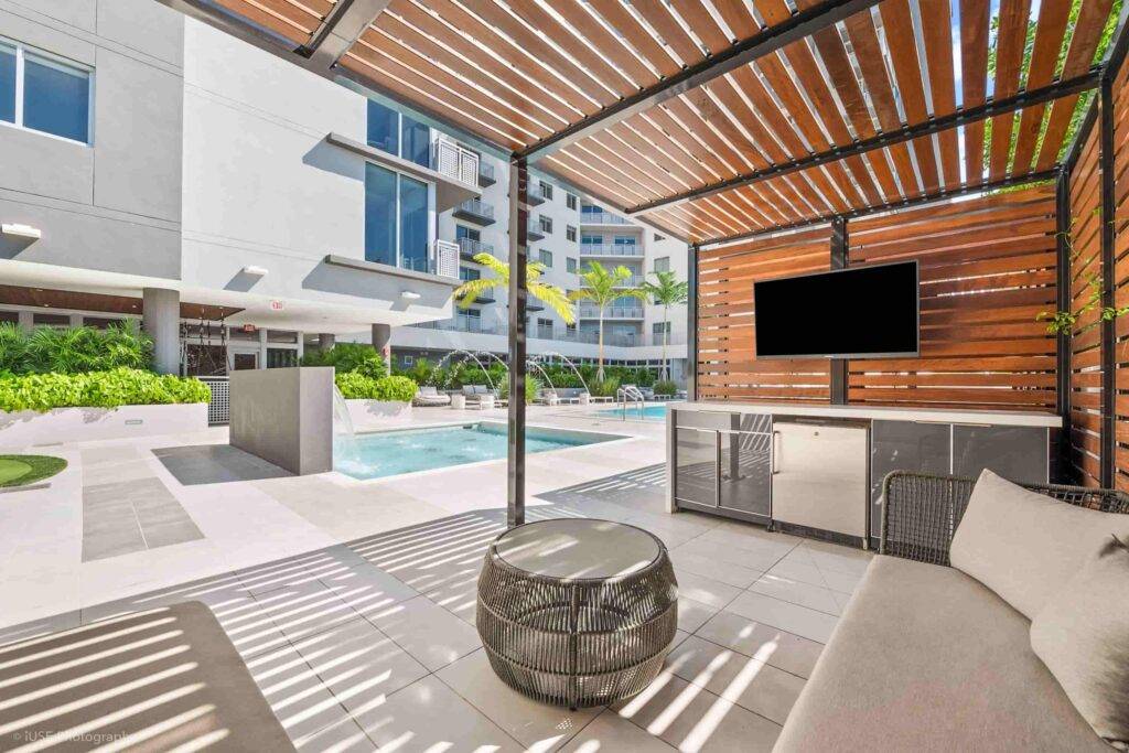 Modern outdoor lounge area with sleek wooden pergola, pool, and TV in a luxury urban setting.