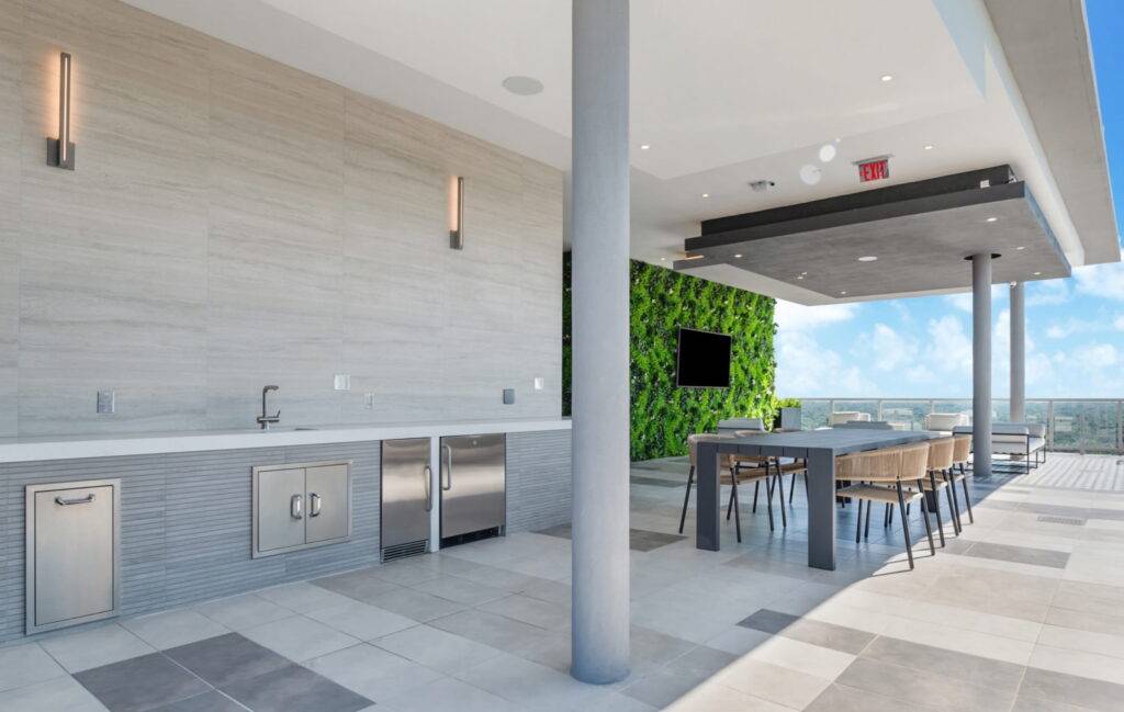 Modern outdoor kitchen with sleek countertops, green wall, and dining area under a covered patio.