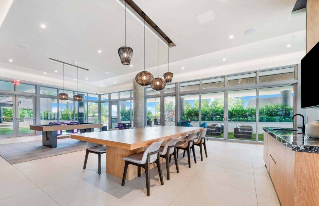 Modern dining area with long wooden table, stylish chairs, and pendant lighting beside floor-to-ceiling windows.