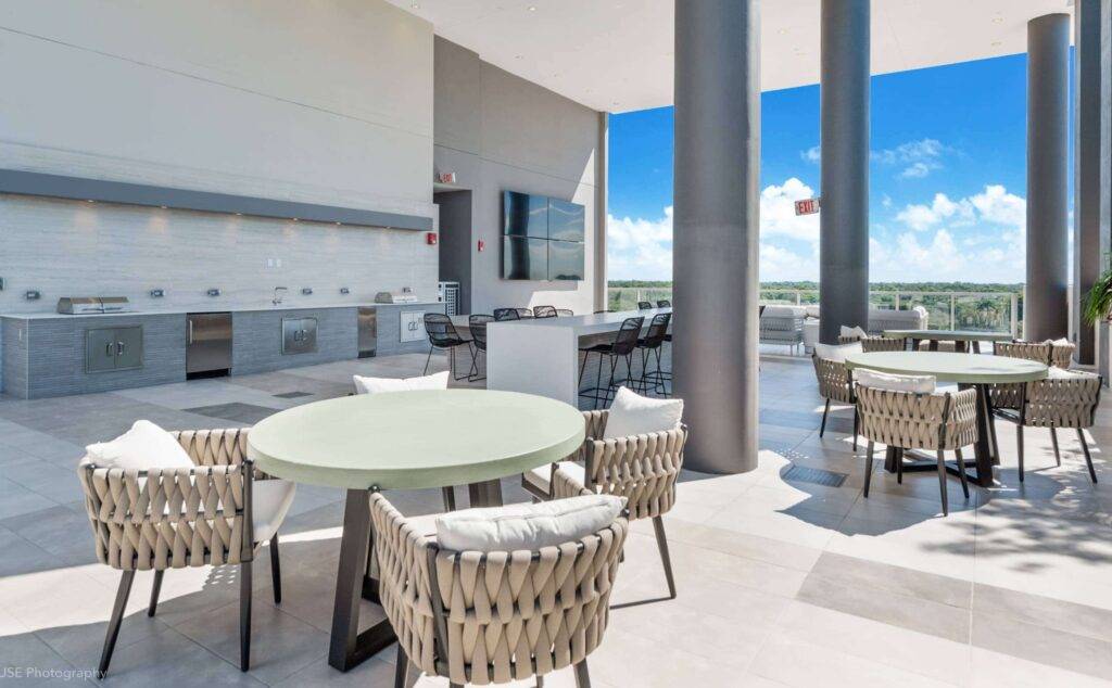Modern outdoor seating area with round tables and woven chairs under a bright sky.