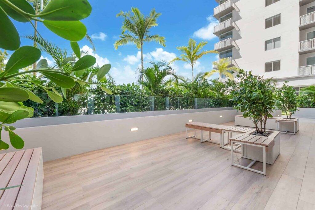 Modern rooftop terrace with lush greenery and palm trees against a bright blue sky.