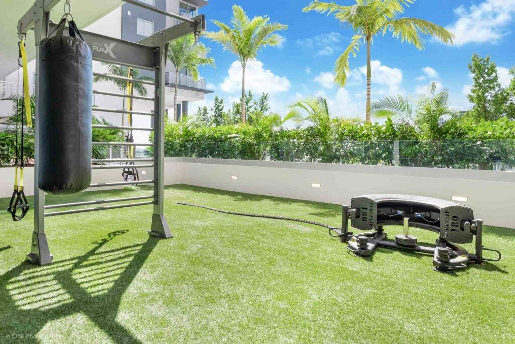 Outdoor gym setup with punching bag and fitness equipment on lush green lawn beneath clear blue sky.