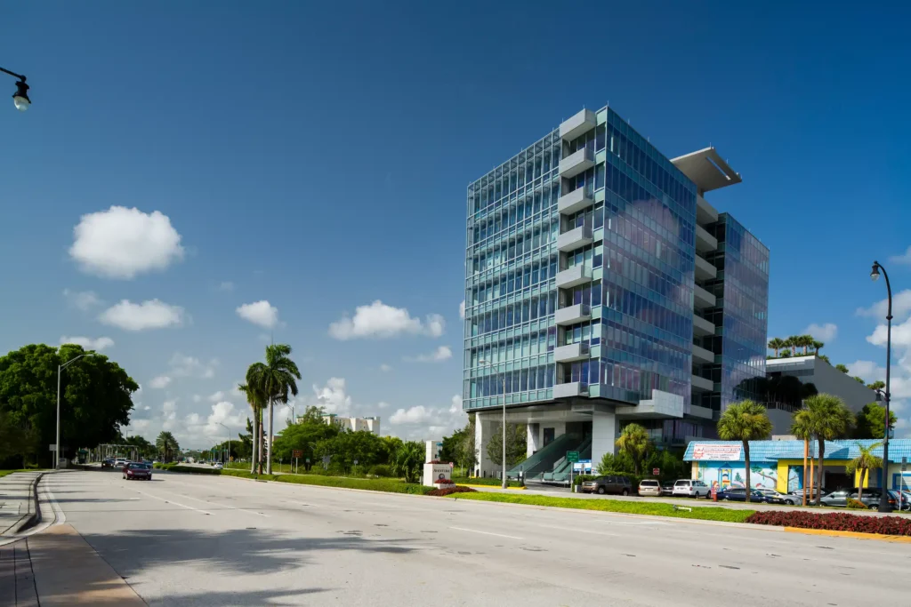 Modern office building with glass facade and palm trees under a clear blue sky