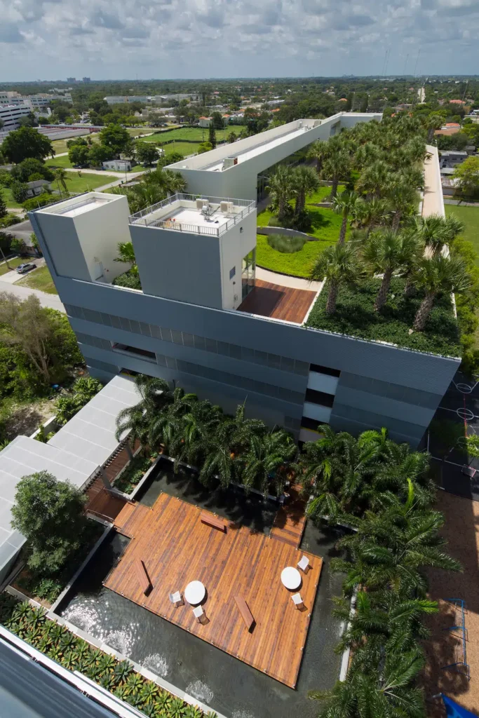 Aerial view of a modern office building with rooftop gardens and outdoor seating areas surrounded by lush greenery.