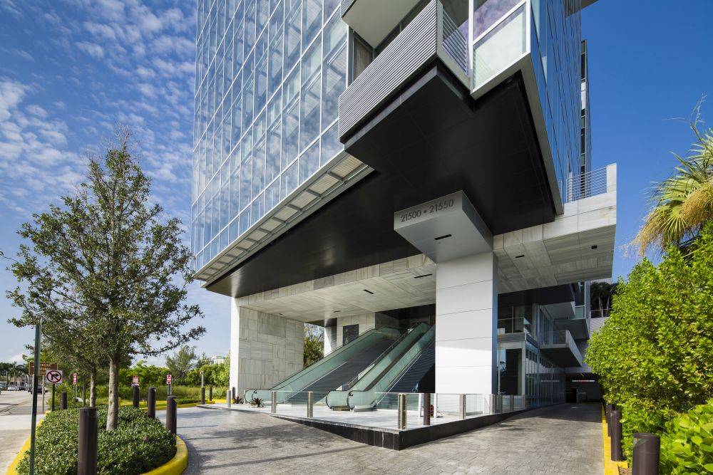 Modern glass building with escalators and lush greenery.