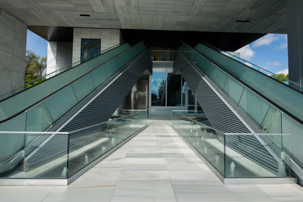 Modern escalators leading to a sleek glass entrance in an urban setting.
