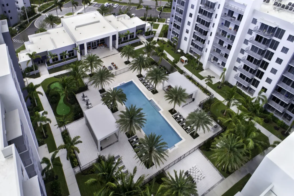 Aerial view of a luxurious apartment complex with a central pool and lush palm trees.