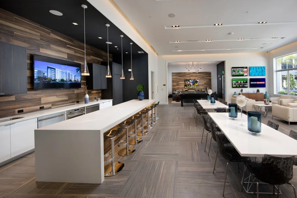 Modern lounge area with sleek design, featuring a long white table, stylish chairs, and wall-mounted TVs.