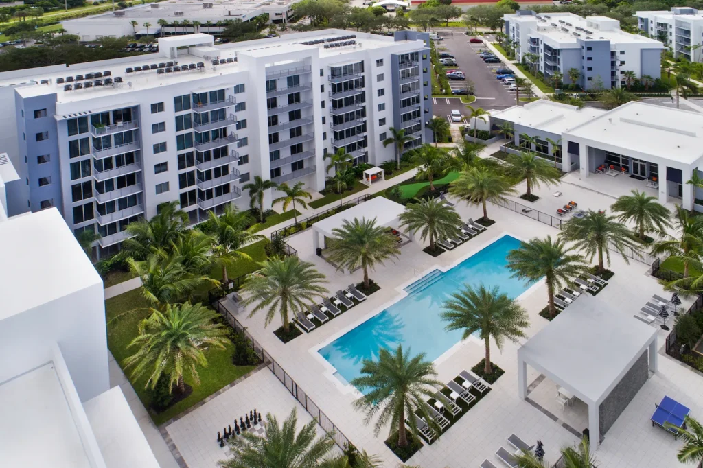 Aerial view of a luxurious resort featuring a pristine pool, surrounded by elegant white buildings and lush palm trees.