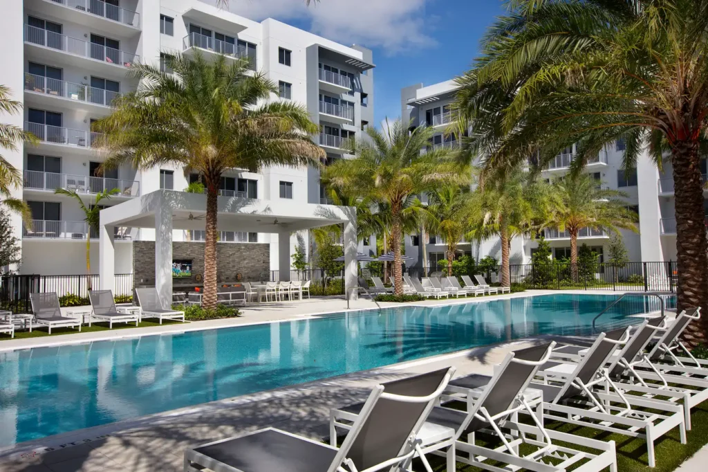 Modern apartment complex with a pool and lush palm trees under a blue sky.