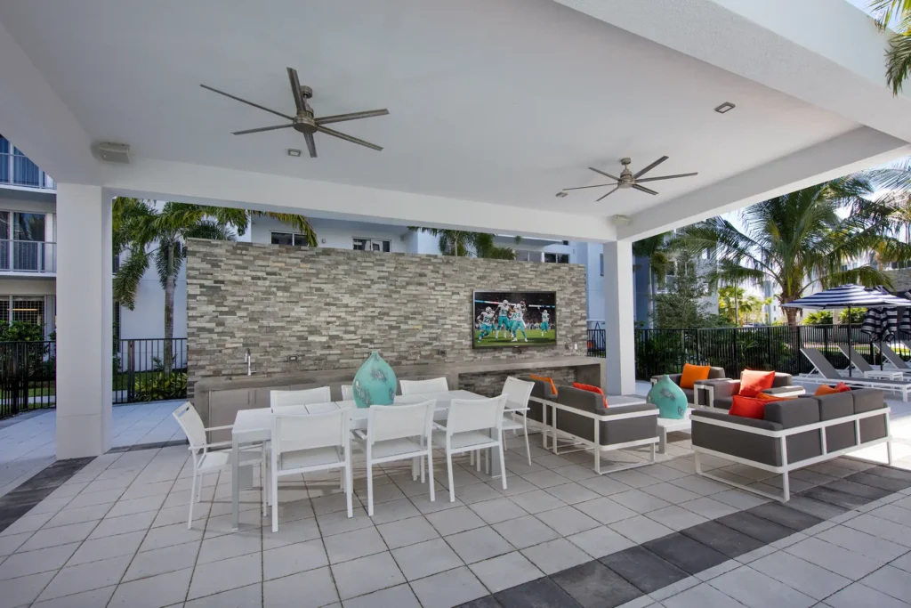Outdoor lounge area with modern furniture, flat-screen TV, and vibrant cushions under a shaded patio.